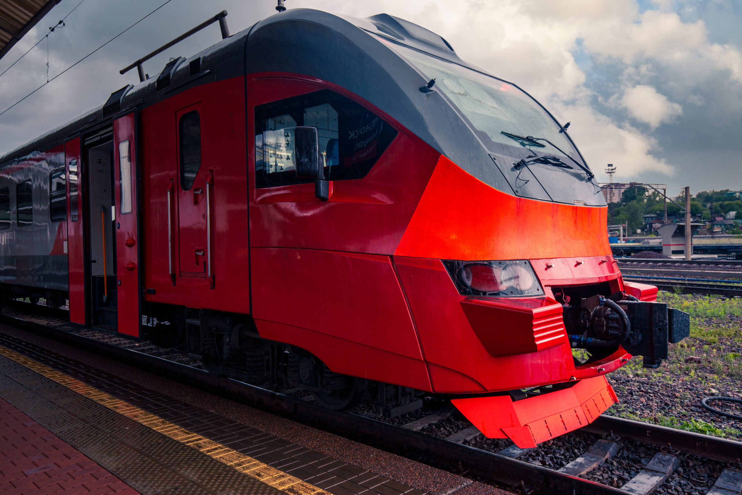 A bright red train stands on the platform of the railway station in the city. Passenger Transportation.